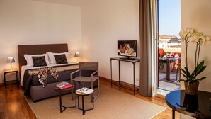 Une chambre d’hôtel avec un lit, une télévision, une petite table, un canapé et un balcon agrémenté de plantes.
