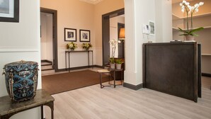 Un hall d’hôtel moderne avec un plancher en bois, un comptoir d’accueil, des œuvres d’art encadrées accrochées aux murs et un coffre décoratif.