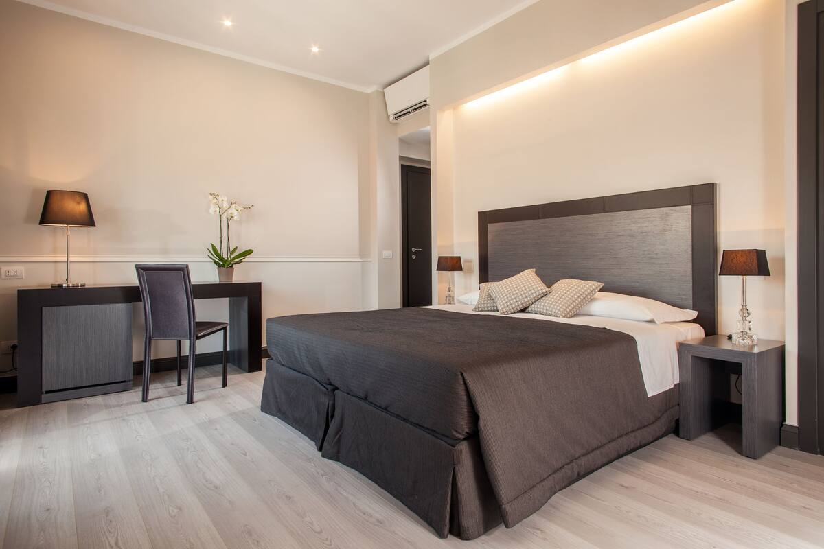 A modern bedroom with a large bed, bedside tables, a desk, and a chair.