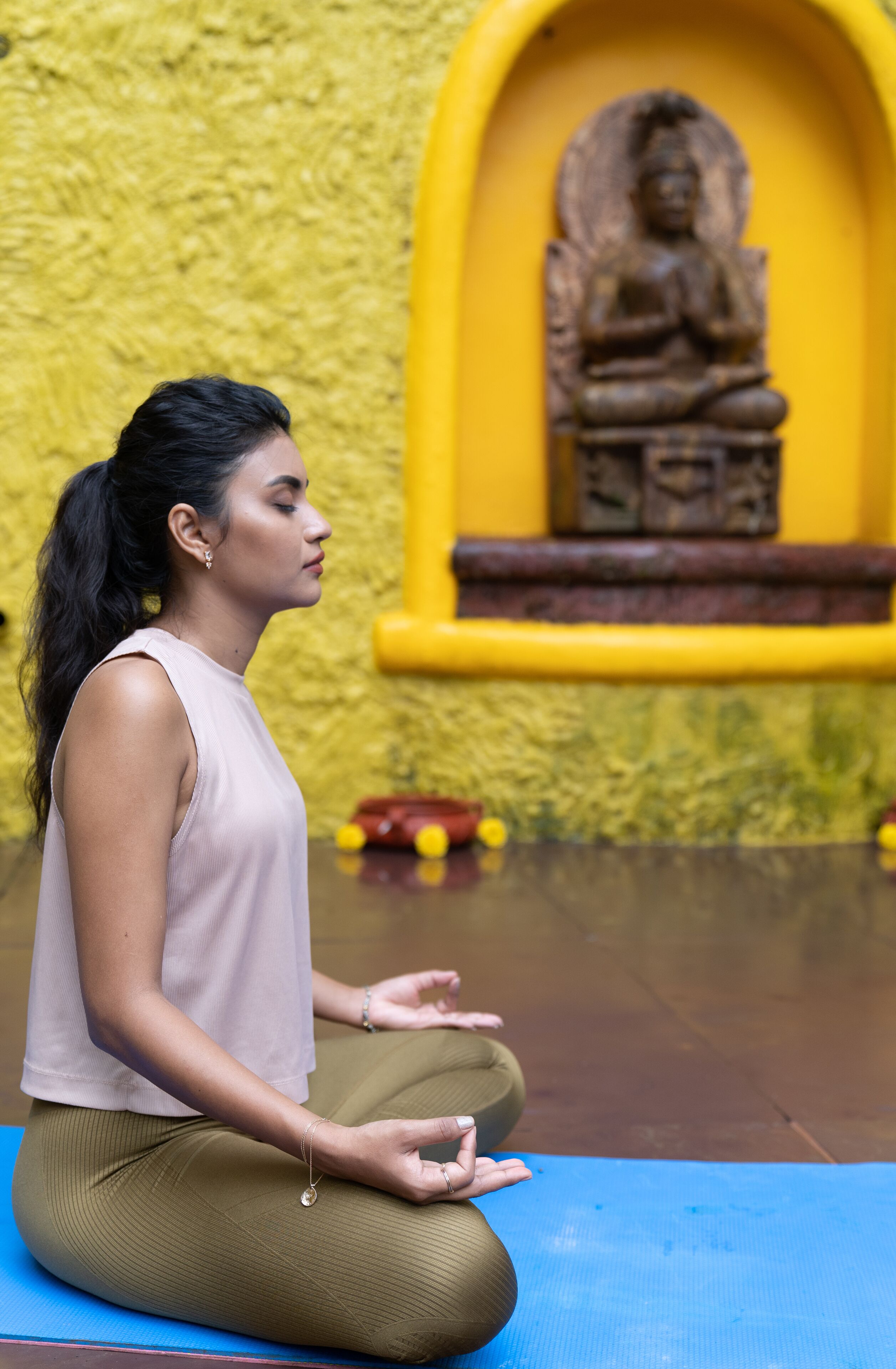 A person sitting on a yoga mat in front of a yellow wall with a statue.