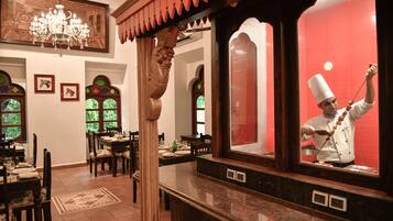 A restaurant interior with wooden furniture, a chandelier, and a chef preparing food.