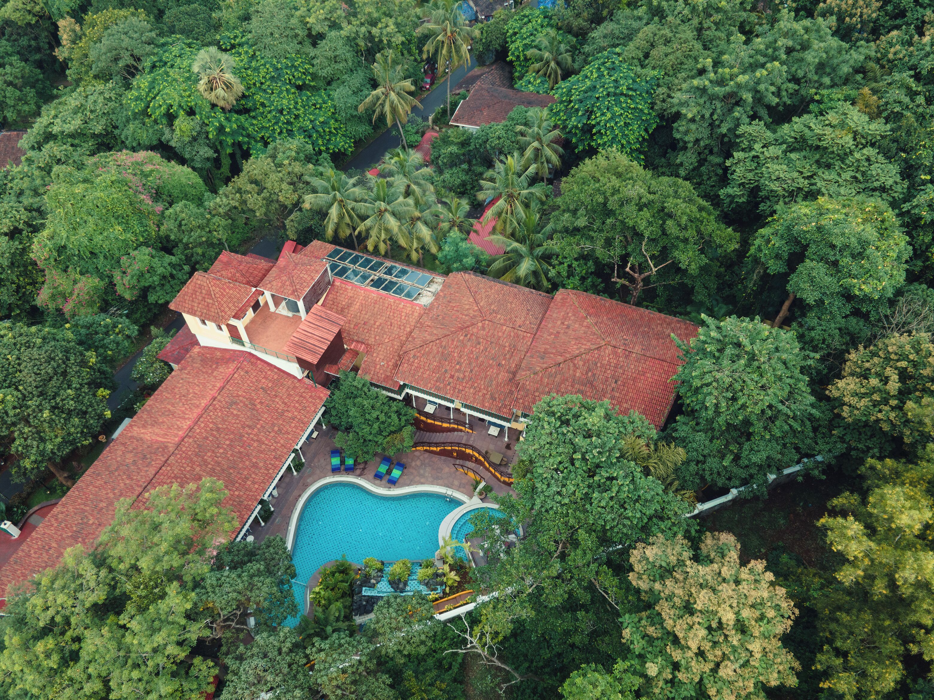 An aerial view of a property with a swimming pool, multiple buildings, and dense surrounding vegetation.