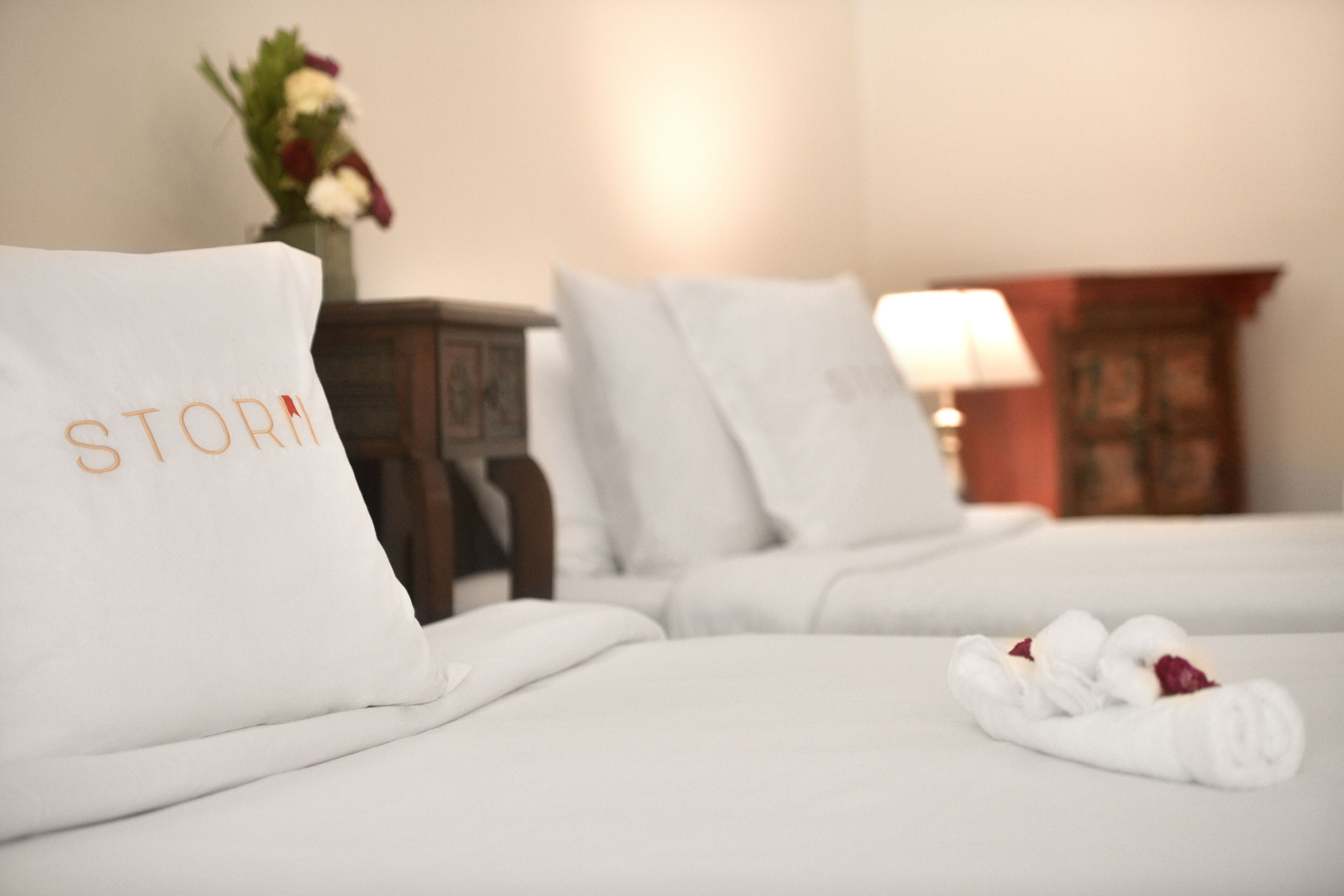 Een hotelkamer met keurig opgemaakte bedden, witte linnens en een bloemstuk op het nachtkastje.