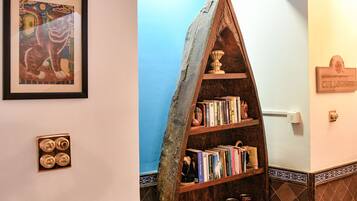 A corner of a room with a wooden bookshelf filled with books and decorative items, a framed picture on the wall, and a tiled floor.