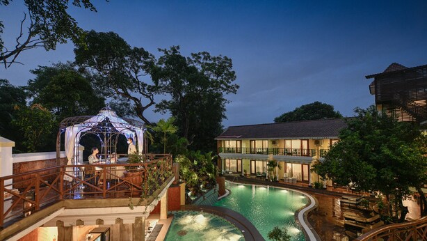 A swimming pool with a curved design, surrounded by wooden deck areas and lounge chairs. - Storii by ITC Hotels Shanti Morada Saligao, Goa (Saligao)