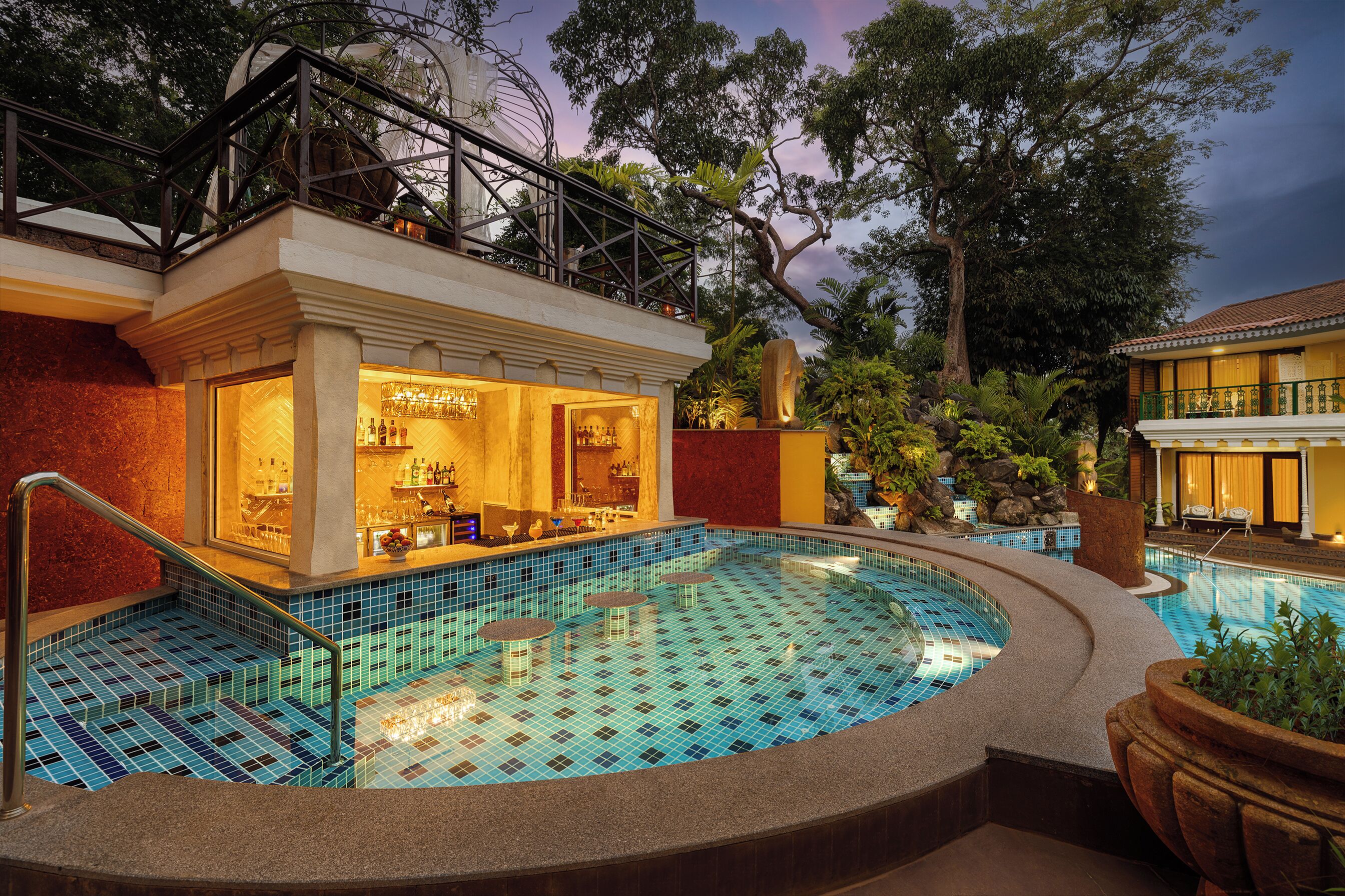 A pool area with a bar and seating, surrounded by trees and a building with a balcony.