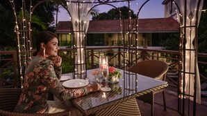 A dining area with a glass table, wicker chairs, and a decorative archway with string lights. - Storii by ITC Hotels Shanti Morada Saligao, Goa (Saligao)