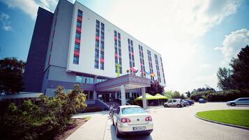 A hotel with a modern design, featuring a prominent entrance with a covered area and multiple flags.