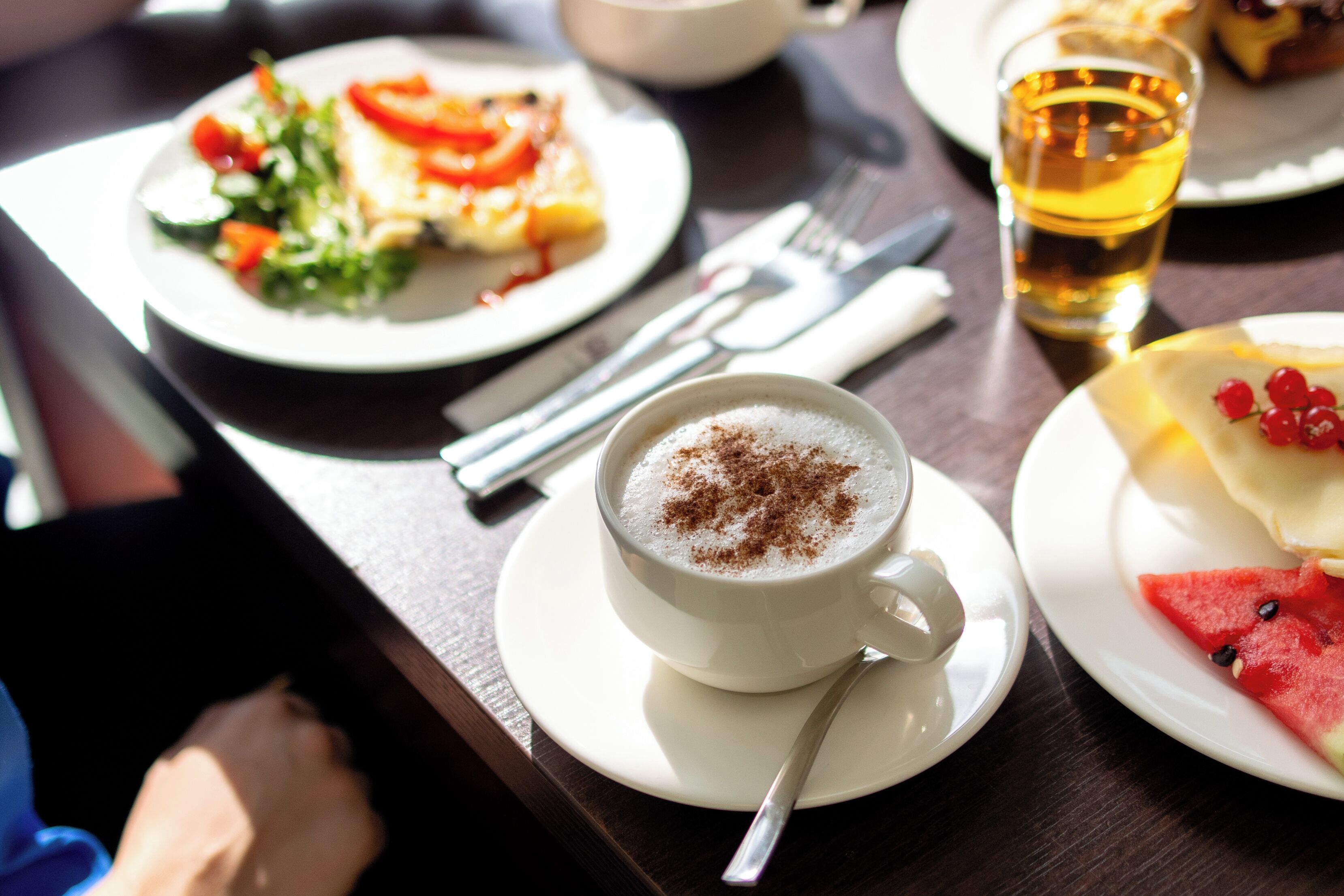 A dining table with a plate of food, a cup of coffee, and a glass of beer.