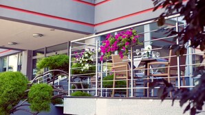 A modern building with a balcony, potted plants, and outdoor seating.