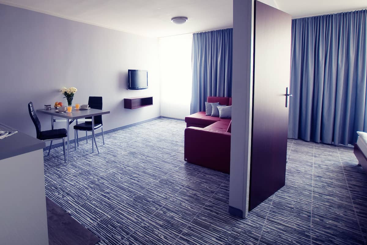 Ett hotellrum med en matplats, en tv som är monterad på väggen, en röd soffa och ett stort fönster med gardiner.