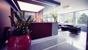 A modern reception area with a glass partition, a reception desk, and a seating area with a sofa and a coffee table.