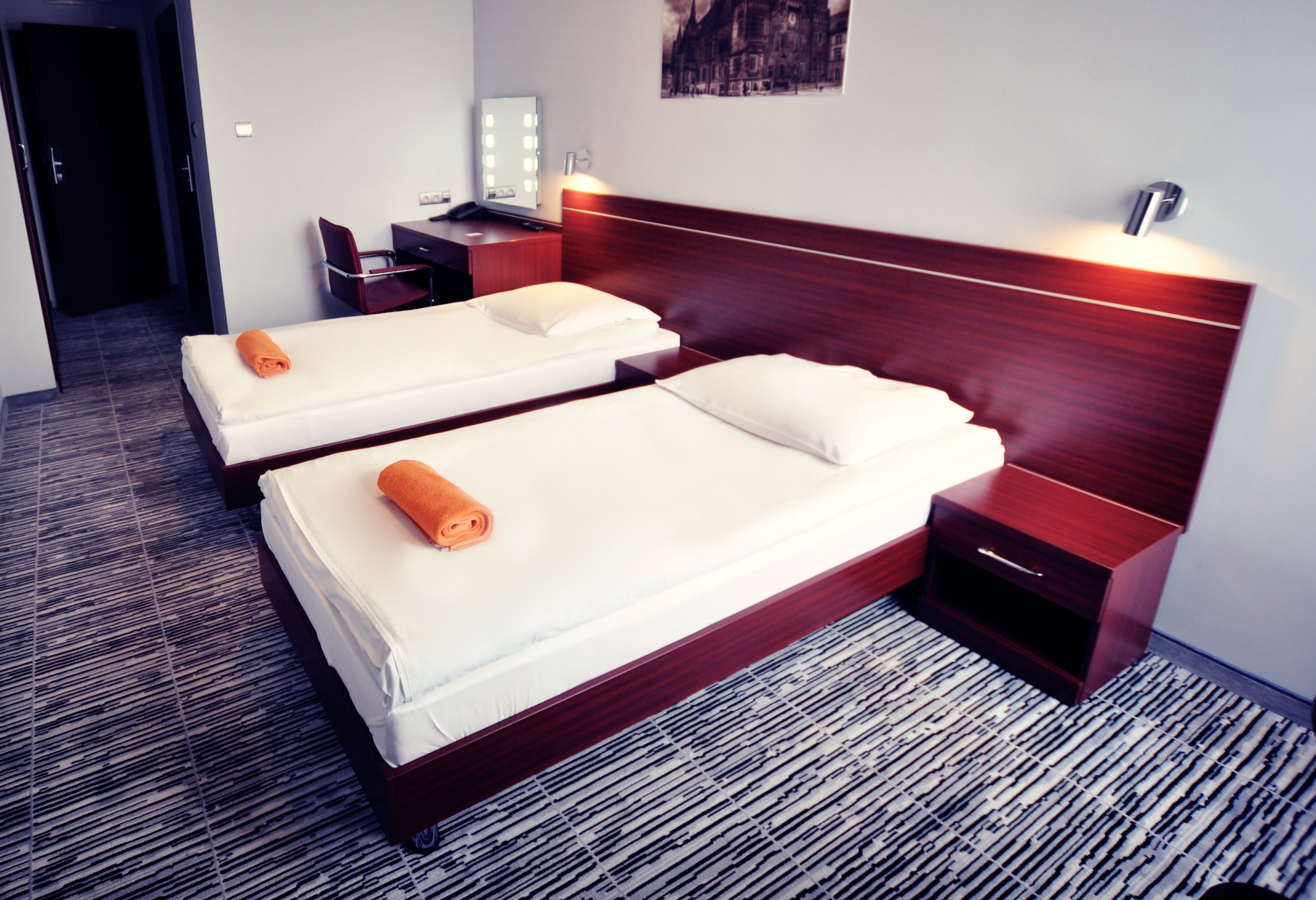 A hotel room with two beds, a desk with a mirror, and a nightstand with a lamp.