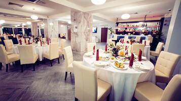 Comedor con mesas redondas dispuestas para una comida, con manteles blancos y servilletas rojas.