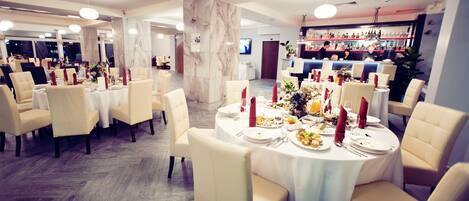 A dining area with round tables set for a meal, featuring white tablecloths and red napkins.