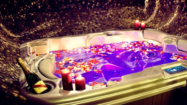 A hot tub with a champagne bottle, two candles, and flower petals.