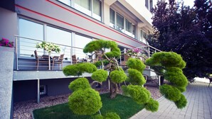 A modern building with a balcony, outdoor seating, and neatly trimmed hedges.