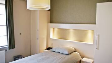A hotel room with a bed, bedside table, lamp, and a small trash bin.