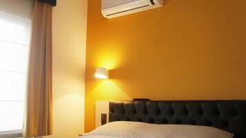 Hotelkamer met een bed, airconditioning, een wandlamp en een raam met gordijnen.