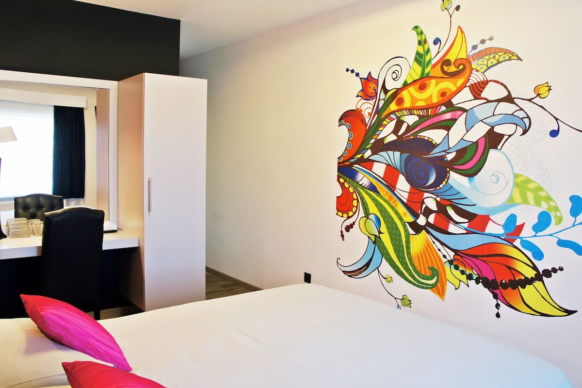A hotel room with a bed, a desk, and a colorful wall mural.
