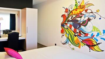 A hotel room with a bed, a desk, and a colorful wall mural.