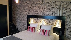 Een hotelkamer met een groot bed, een hoofdeinde met verlichting en een wenteltrap, met behang met een patroon.
