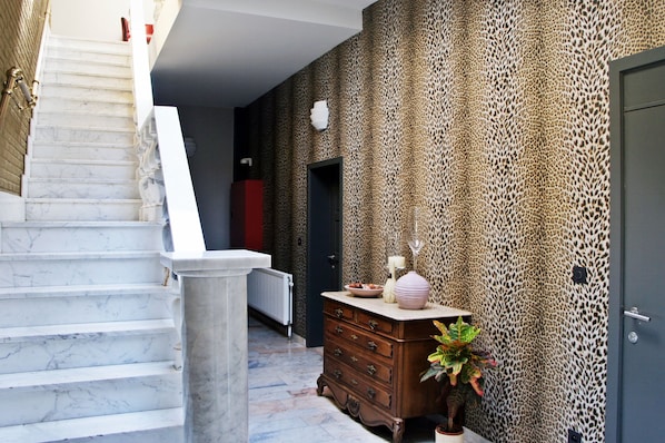 Un pasillo con una escalera de mármol, pared con estampado de leopardo, cómoda de madera y una puerta.