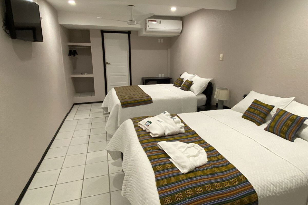 A hotel room with two beds, a TV, an air conditioning unit, and a door leading to a bathroom.