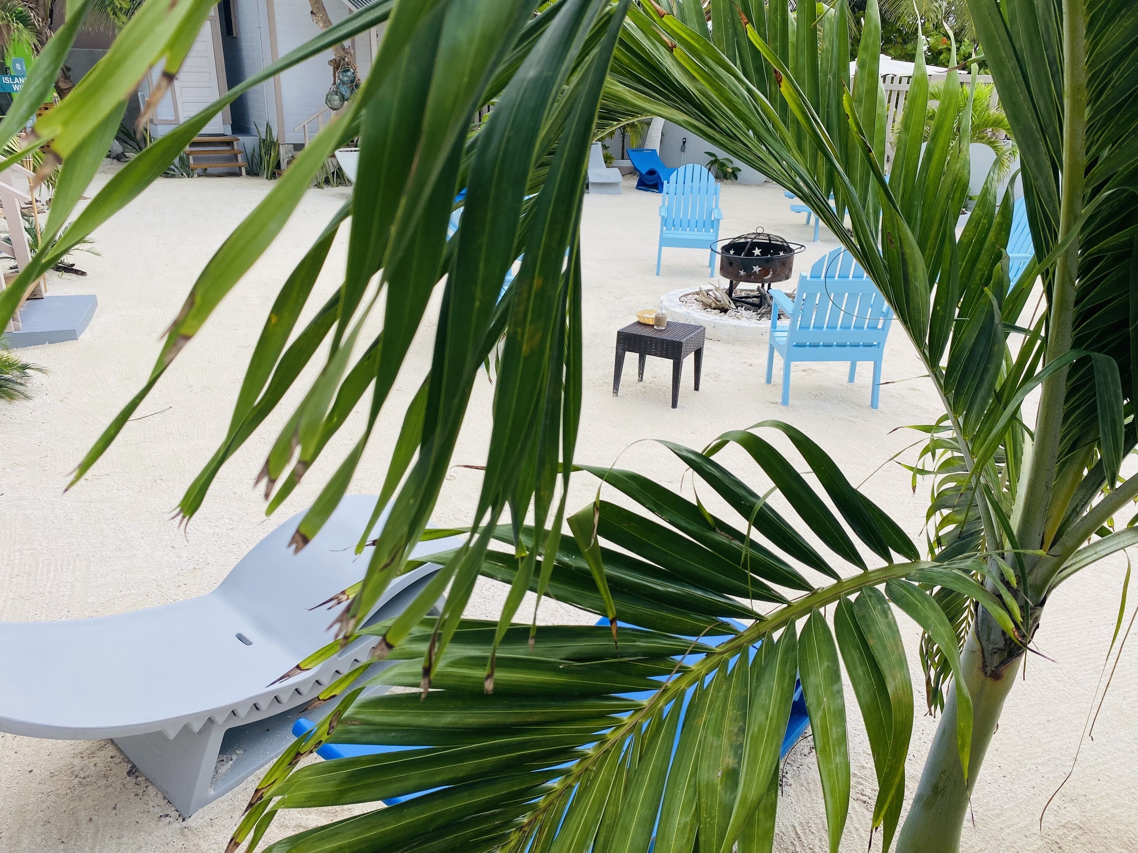Uma área à beira-mar com cadeiras azuis, uma mesa pequena e um espaço para fogueira.