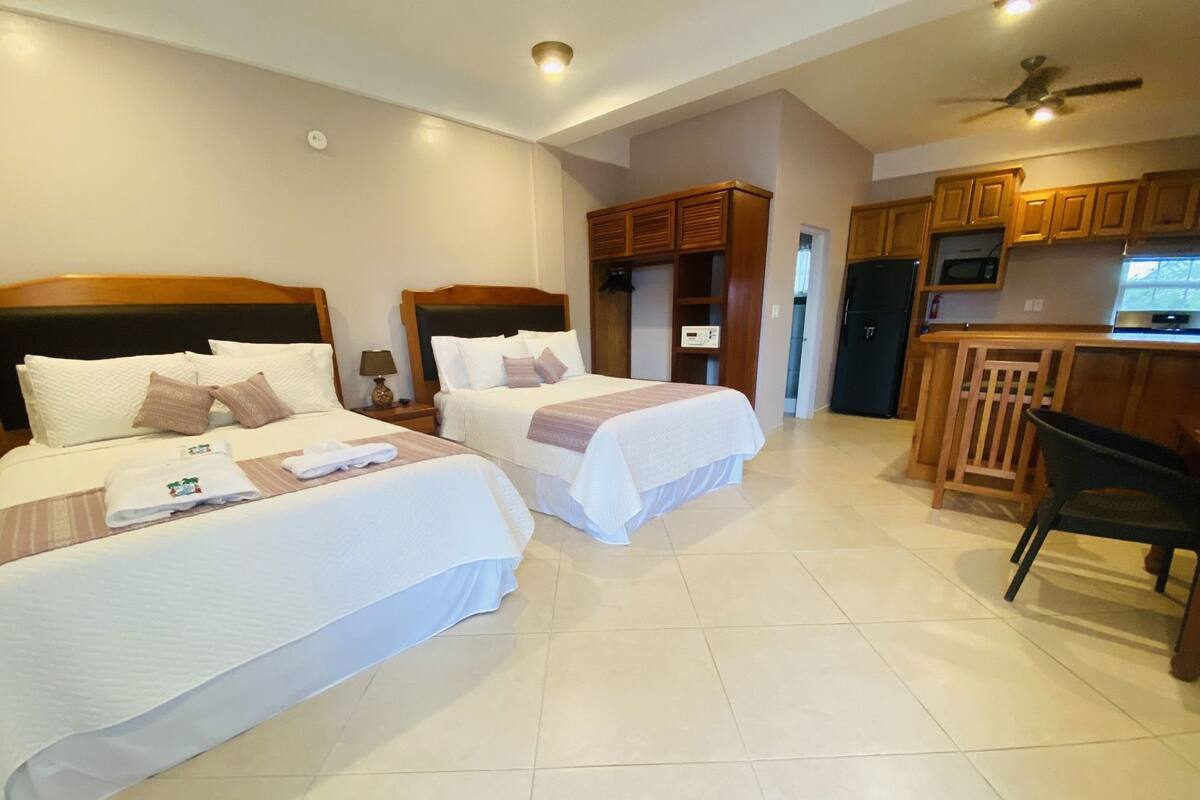 A hotel room with two beds, a kitchenette, and a ceiling fan.