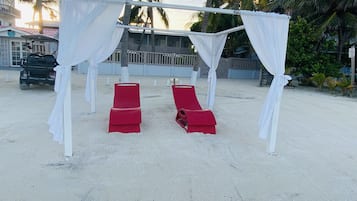 Un paisaje playero con una estructura tipo sombrilla, dos sillones reclinables rojos y un carrito de golf.