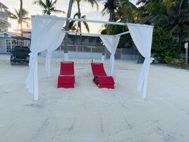 Un paisaje playero con una estructura tipo sombrilla, dos sillones reclinables rojos y un carrito de golf.