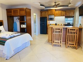 Habitación de hotel con cama, kitchenette, armarios de madera y ventilador de techo.