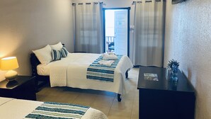 A hotel room with a bed, a desk, a lamp, and a view of the outside. - La Isla Resort (Caye Caulker)