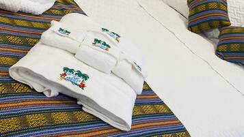 Una cama bien tendida con un colorido edredón a rayas, una almohada blanca y una toalla blanca doblada con motivos tropicales.