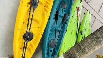 Trois kayaks de couleurs différentes (jaune, bleu et vert) sont appuyés contre un mur.