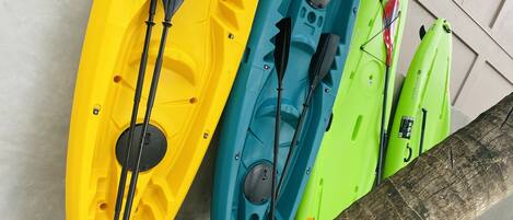 Three kayaks of different colors (yellow, blue, and green) leaning against a wall.
