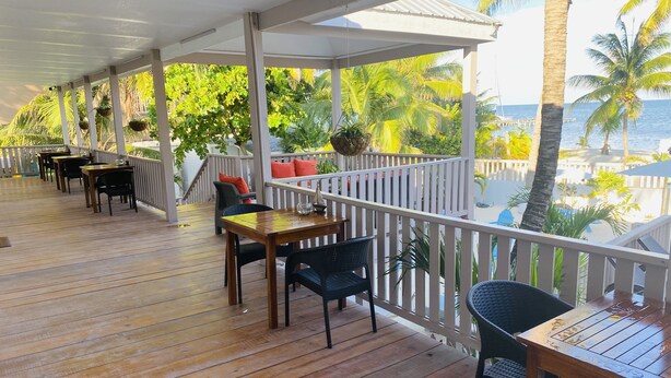 A covered outdoor area with wooden flooring, tables, chairs, and potted plants. - La Isla Resort (Caye Caulker)