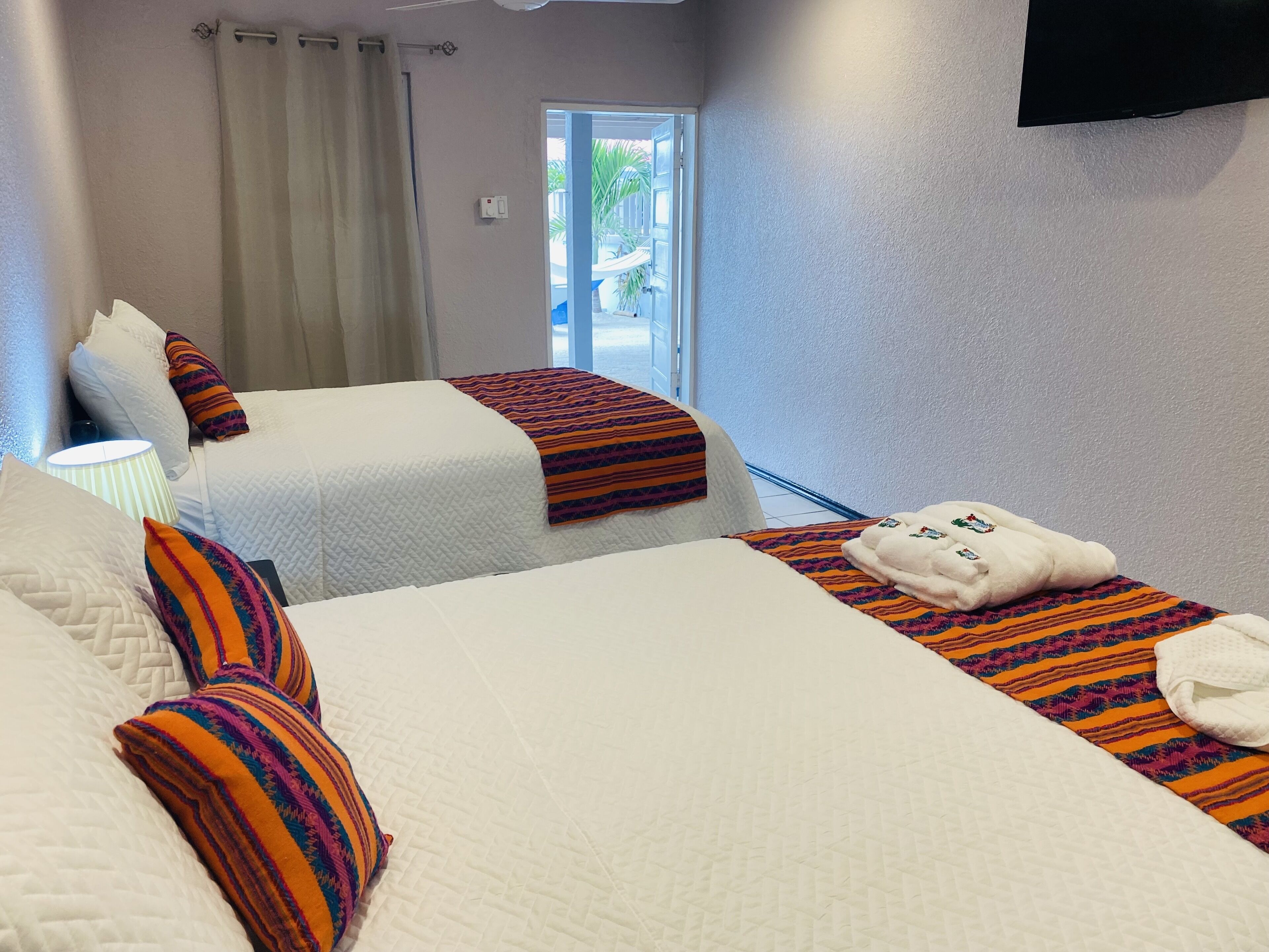 A hotel room with two beds, a TV, a window with a view, and a door leading outside.
