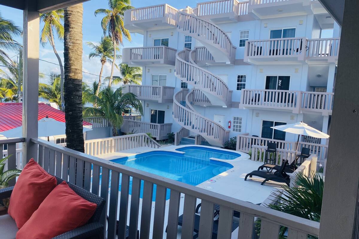 A multi-story building with a central swimming pool, outdoor seating, and palm trees.