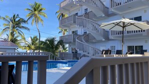 A modern hotel with a pool, outdoor seating, and palm trees. - La Isla Resort (Caye Caulker)