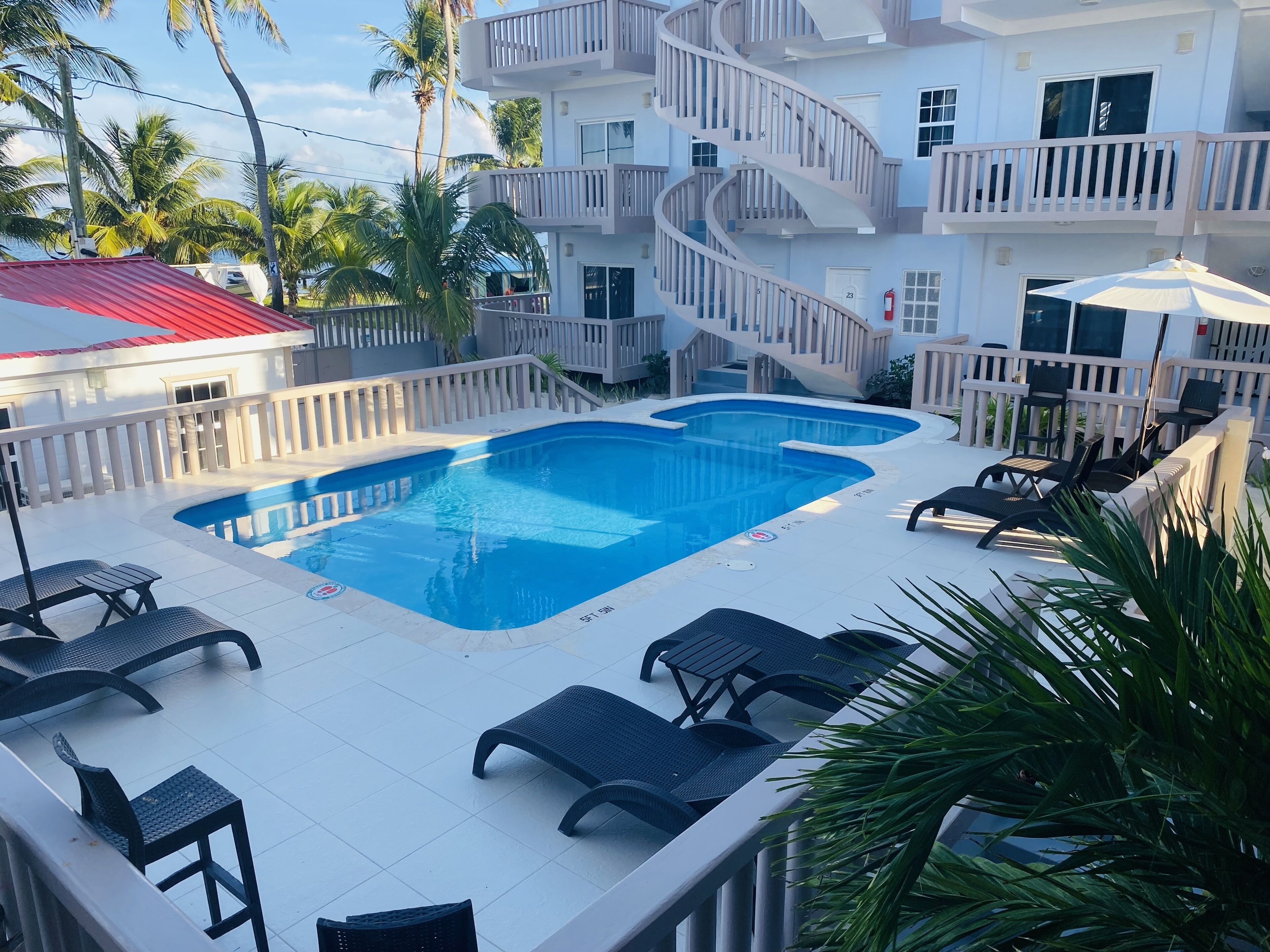 A pool area with lounge chairs and a staircase leading to a balcony.