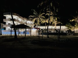 A multi-story building with balconies, a covered area, and palm trees.