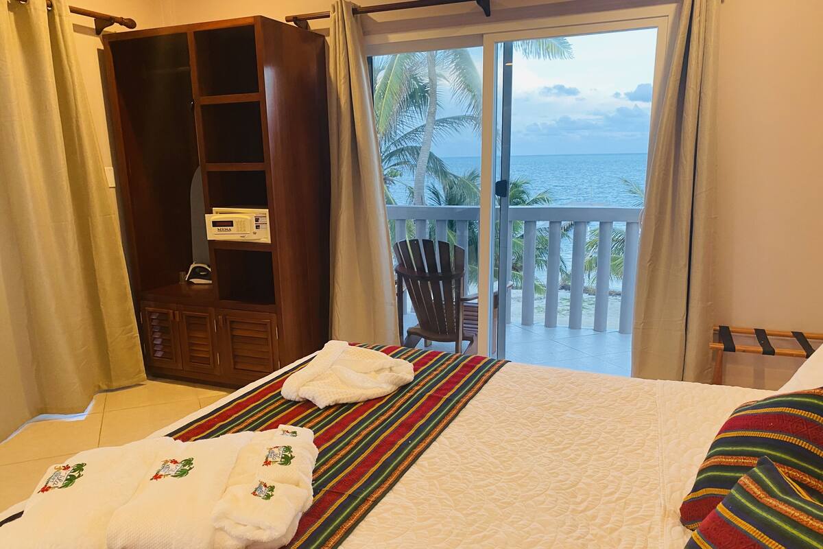 A hotel room with a bed, a wooden wardrobe, a microwave, and a view of the sea.
