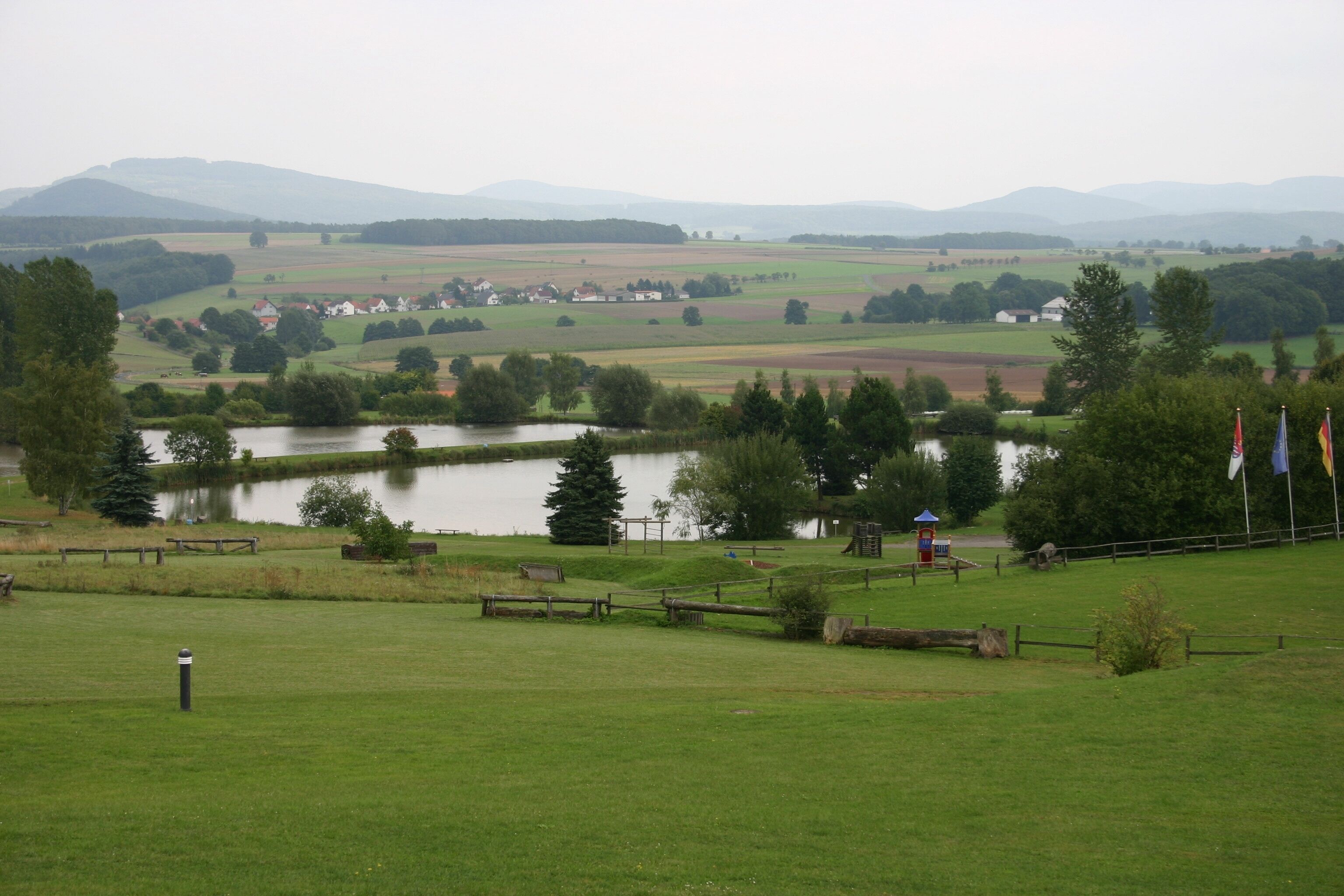 Paisaje rural con un lago, campos y colinas distantes.