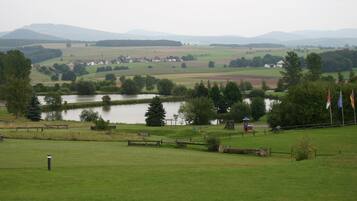 Paisaje rural con un lago, campos y colinas distantes.