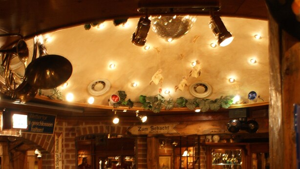A rustic interior with a large wooden wheel, brick walls, and a bar area with shelves of glassware. - Hessen Hotelpark Hohenroda (Hohenroda)