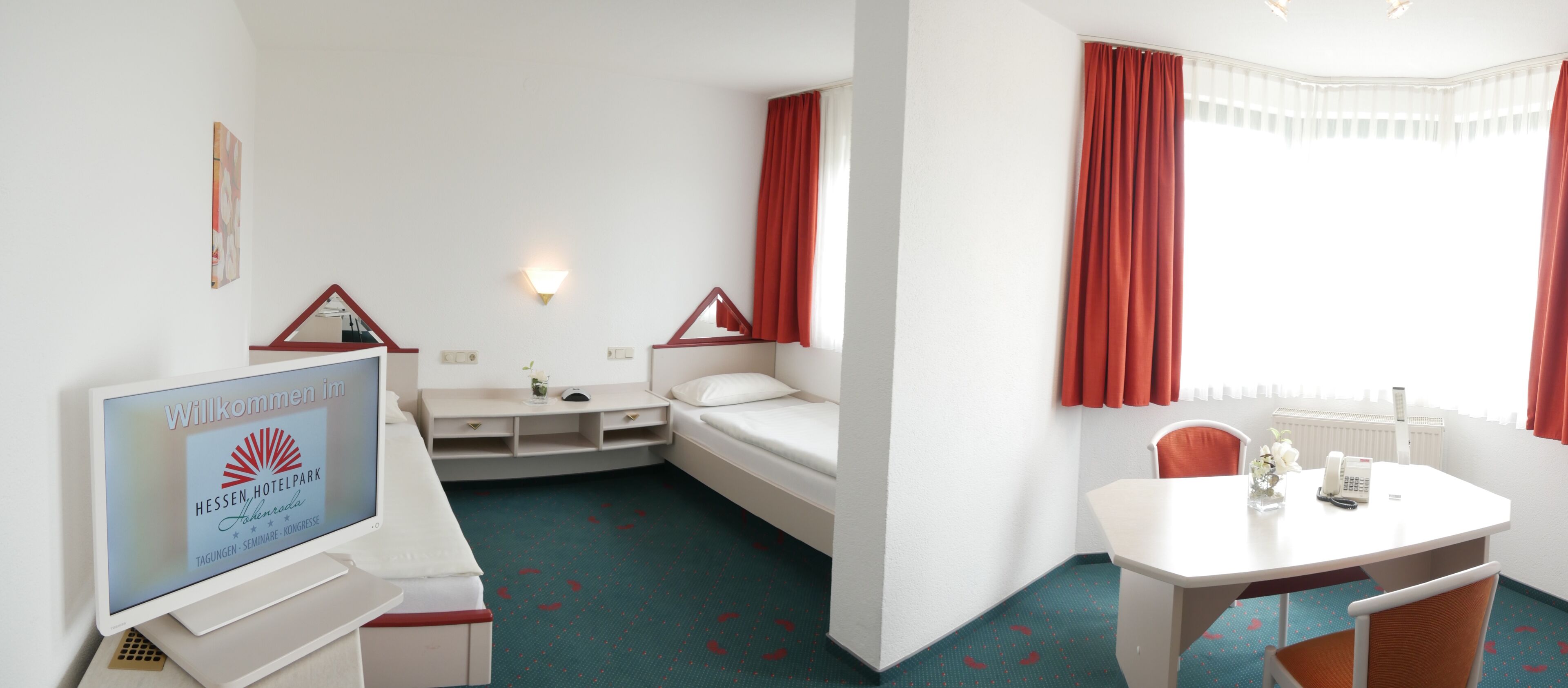 A hotel room with a bed, a desk, a chair, a TV, and a window with curtains.