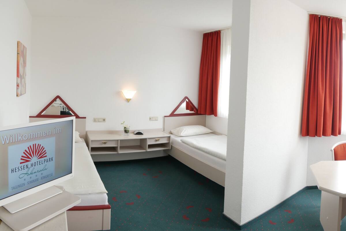 A hotel room with a bed, a desk, a chair, a TV, and a window with curtains.