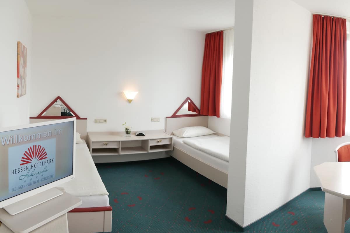 A hotel room with a bed, a desk, a chair, a TV, and a window with curtains.